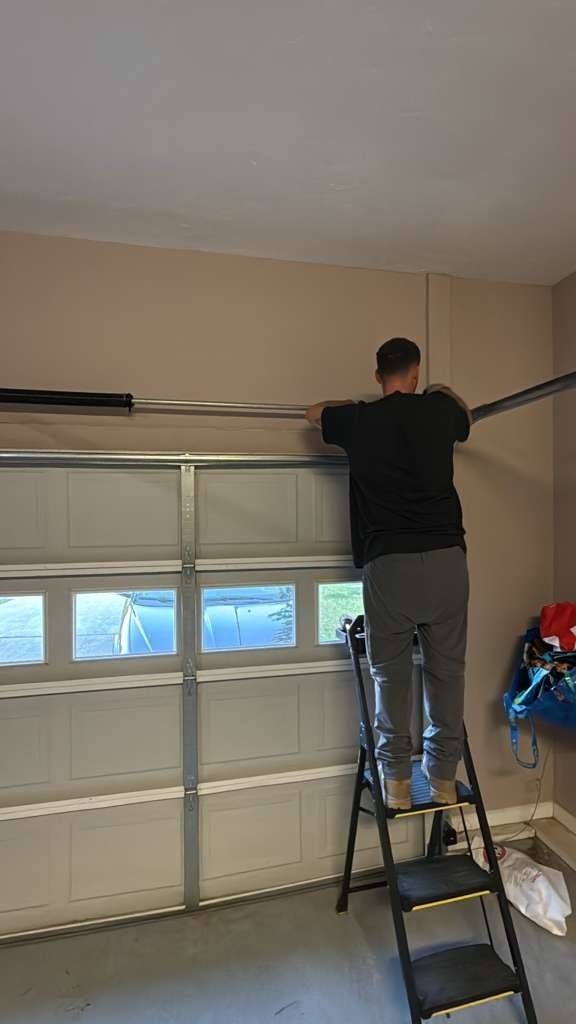 Technician on a step ladder reaching the top section of a closed door with a row of small windows
