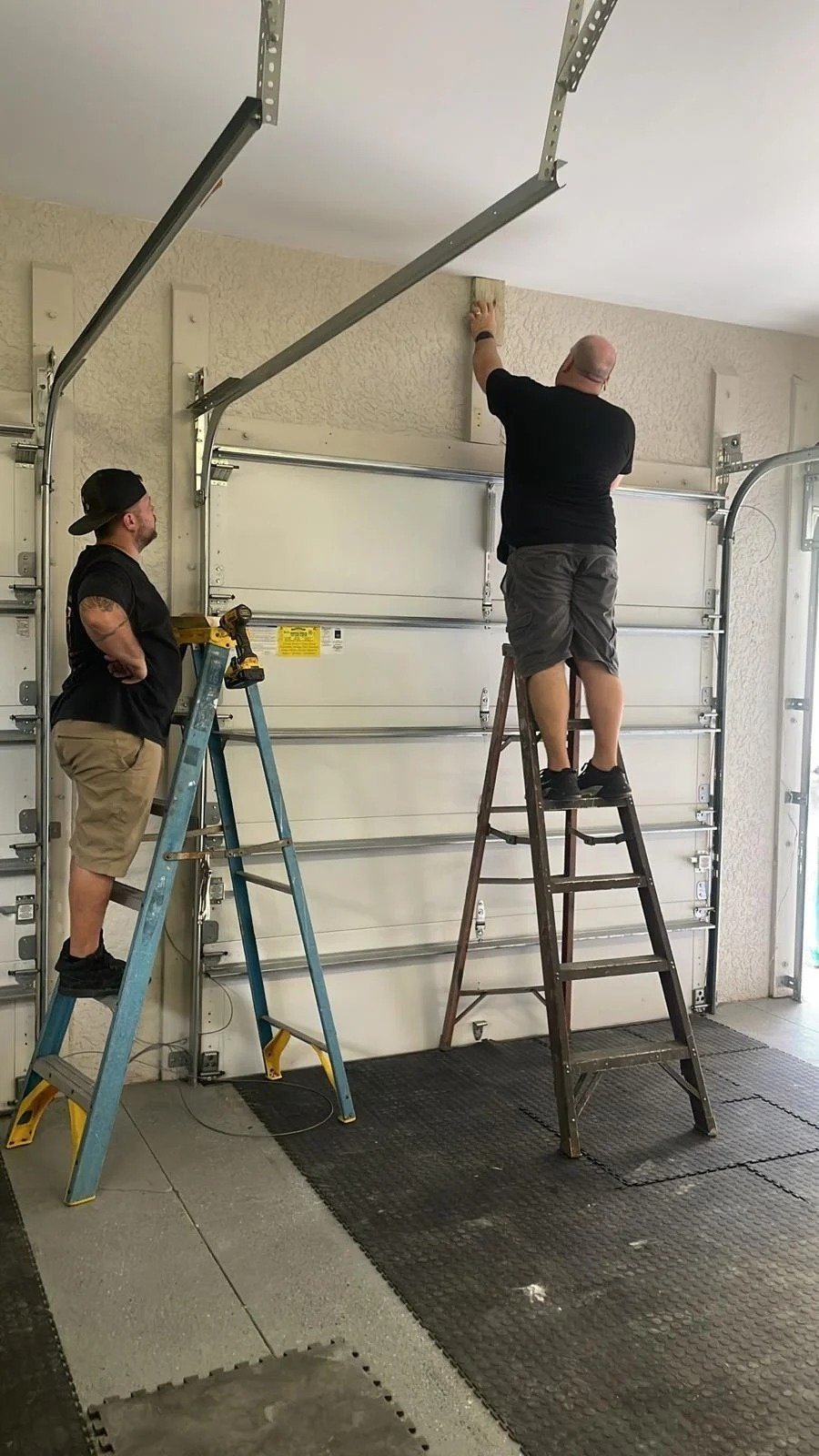 Two technicians on ladders at the top of a garage door