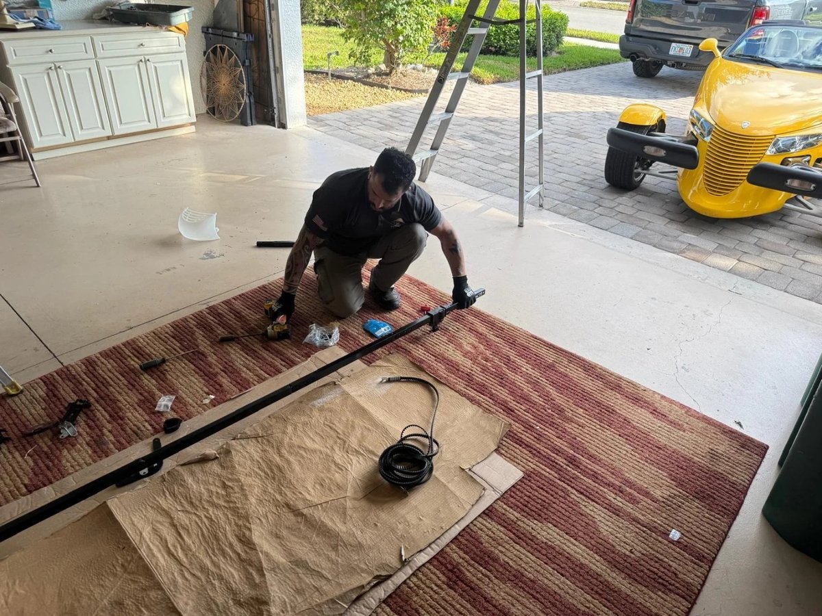 Technician laying out track sections on a rug in a driveway beside a ladder