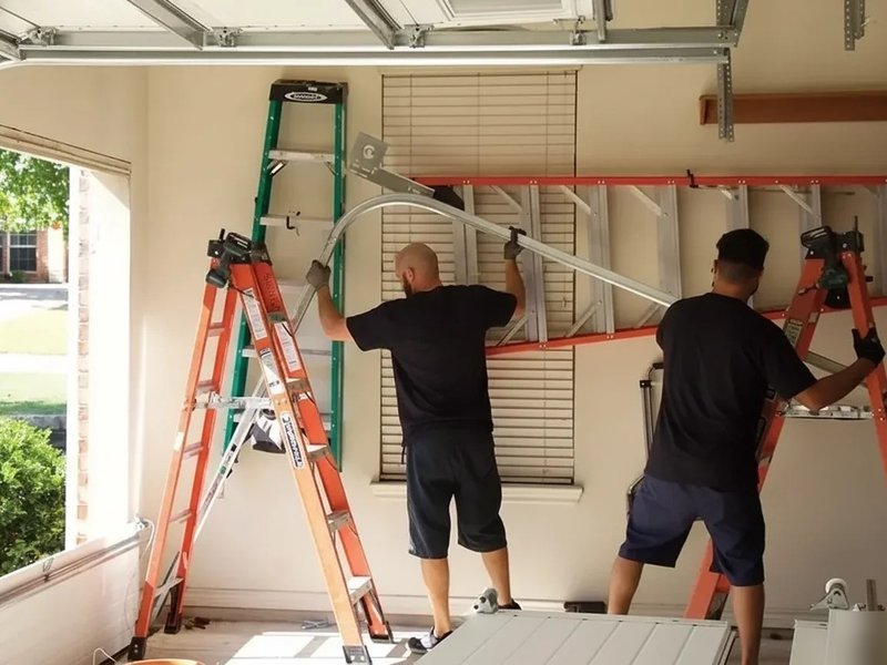 Two technicians on orange ladders working at the header of a garage door
