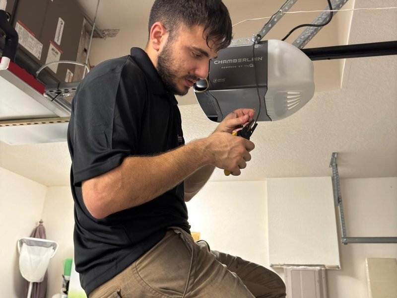 Technician checking wires beneath a ceiling-mounted opener