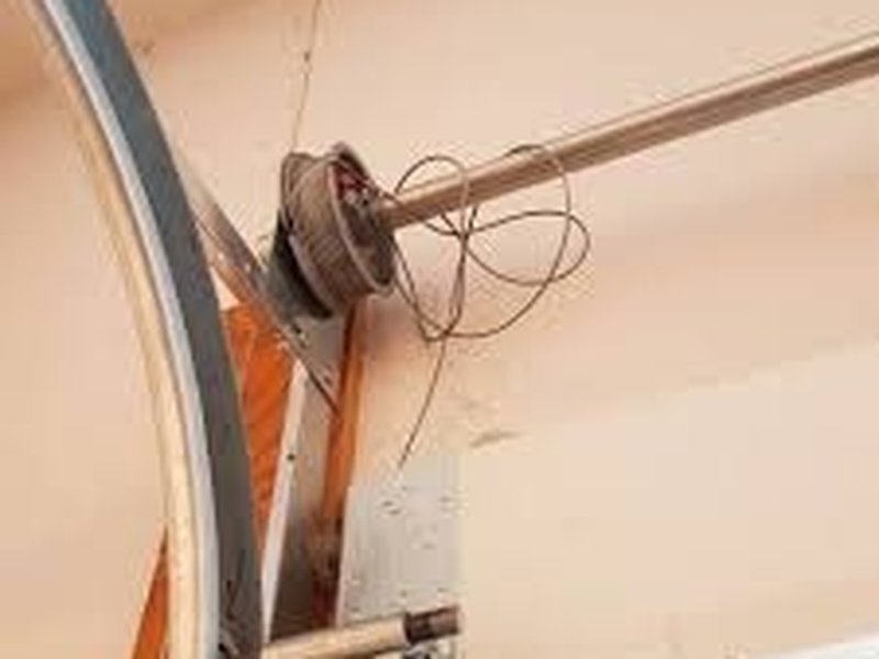 Cable drum with loose cable strands at the end of a torsion shaft beside the door track