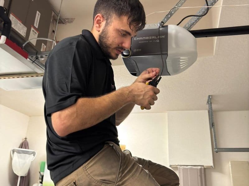 Technician working on an opener motor head above a garage door