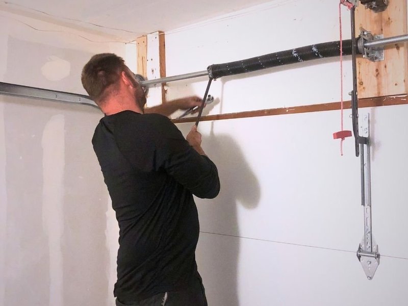 Technician working on a torsion spring with winding bars above a garage door