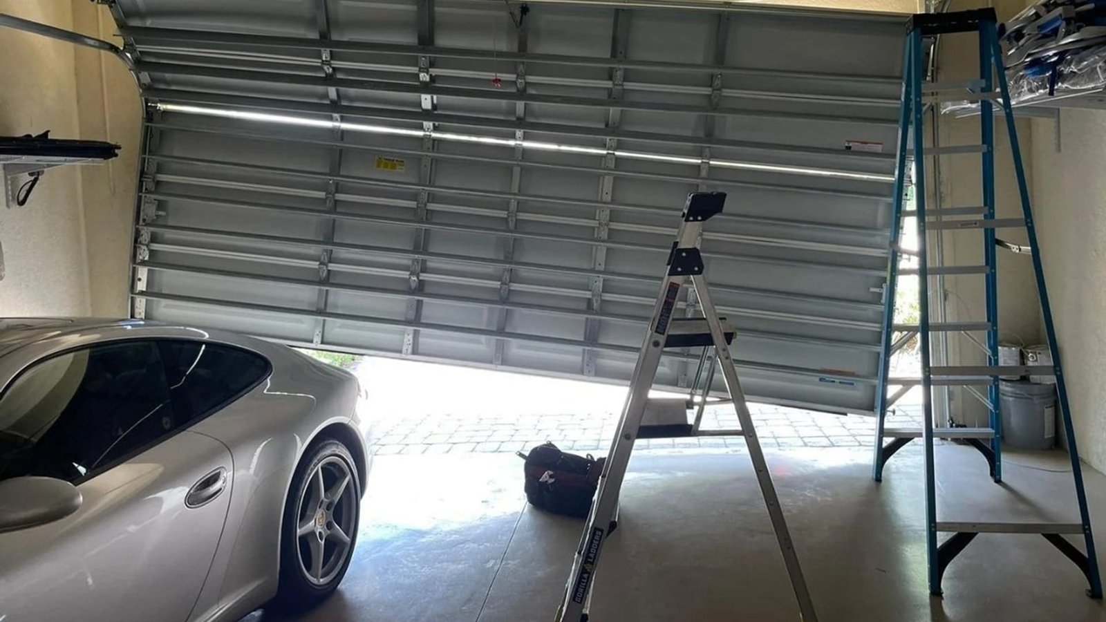 Raised sectional garage door with a ladder beside a parked car